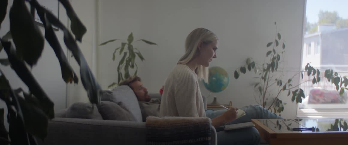 A woman sits on a couch with a pen and paper next to her husband with an infant baby