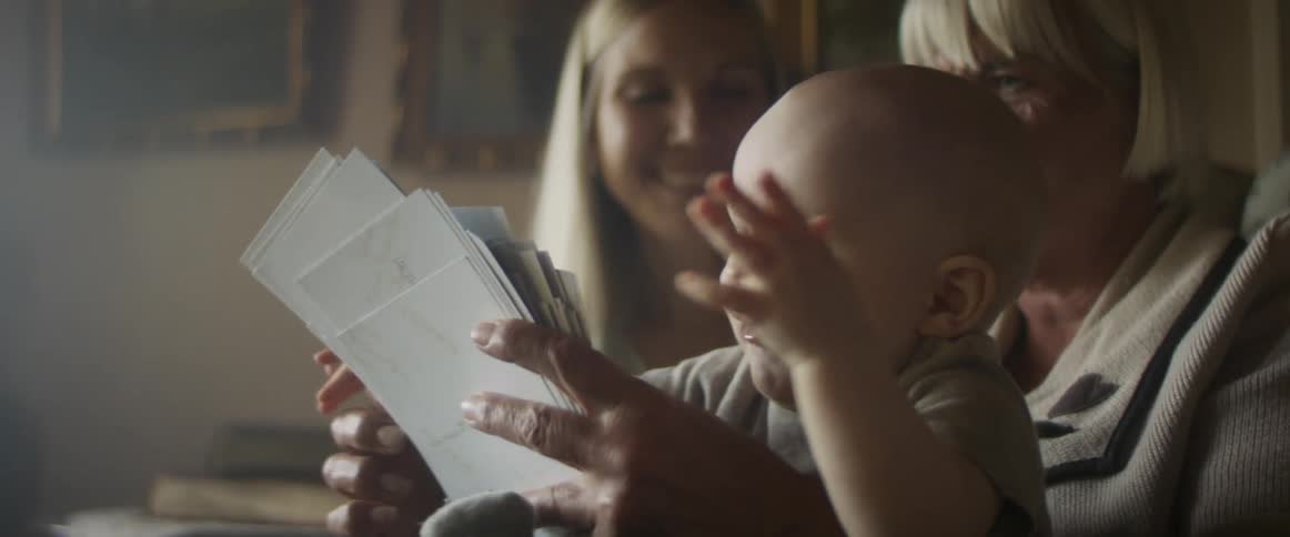 Grandmother shows photographs to her daughter and baby grandson in the living room at home