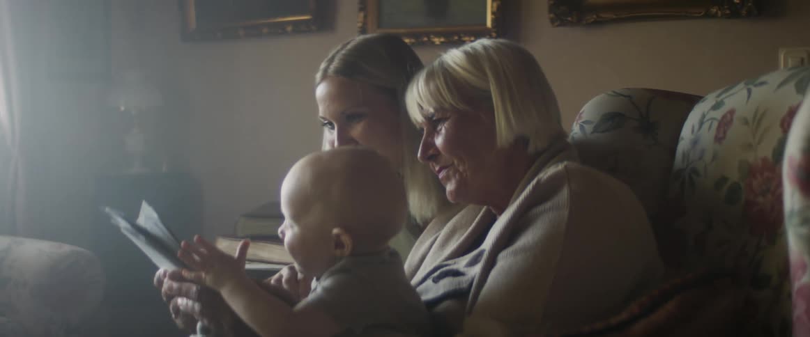 Mother and grandmother sits in the couch with a child looking at photographs