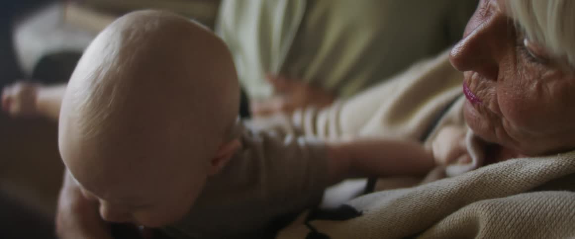 A grandmother holds her grandson and laughs and plays with him when he starts to cry and her daughter sitting next to her gets up