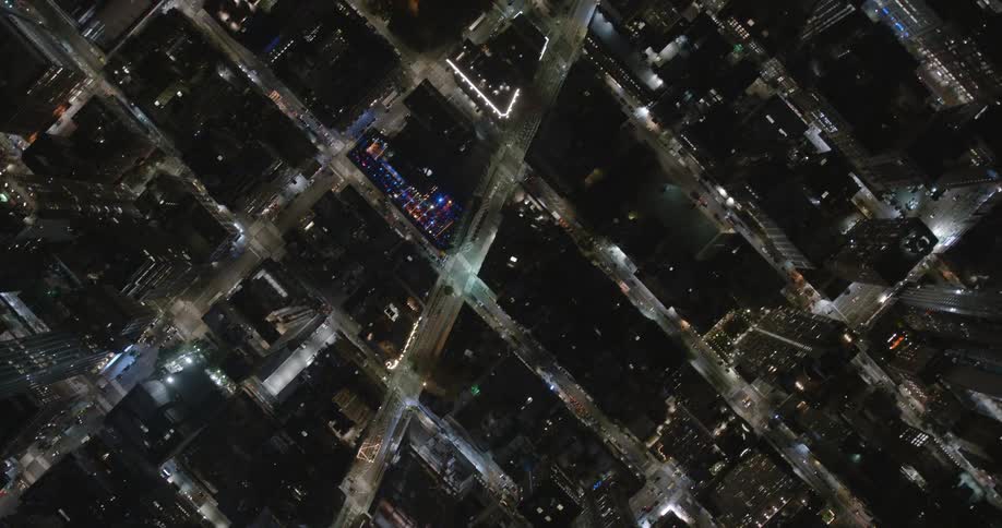 Traffic flows down city streets past skyscrapers at night