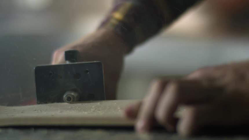 A person in a room using an electric tool to shave a piece of wood