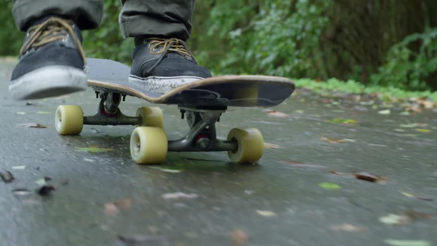 Person skateboards along wet road through woods