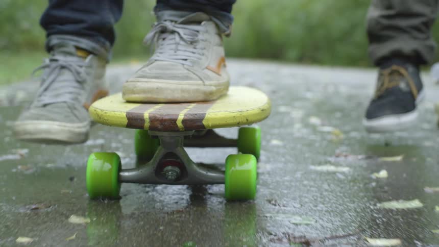 A pair of skateboarders ride their skateboards down a moist road during the day