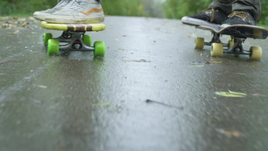 Two people are skateboarding on the wet road