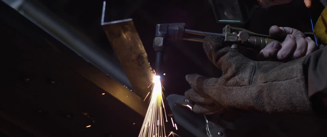 Industrial glove holds welding torch ignited on a piece of metal