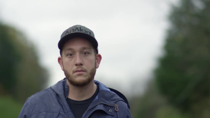 Man wearing baseball cap and jacket walks past trees