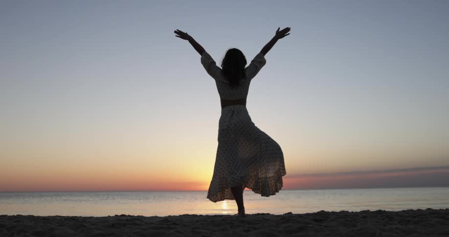 A woman stands on a beach in a yoga pose at sunrise