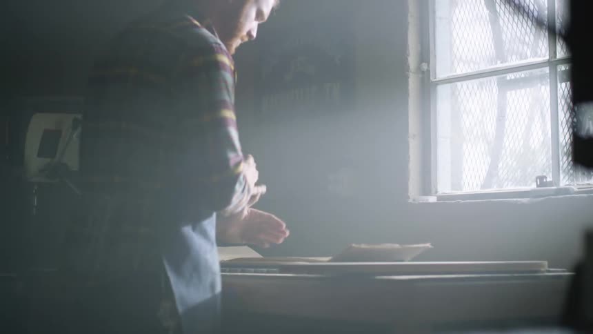 A man in a plaid shirt and apron working with lumber in a workshop