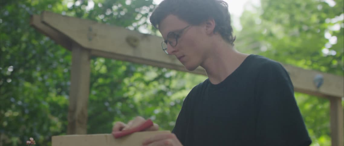 A teenage boy sanding wood outside