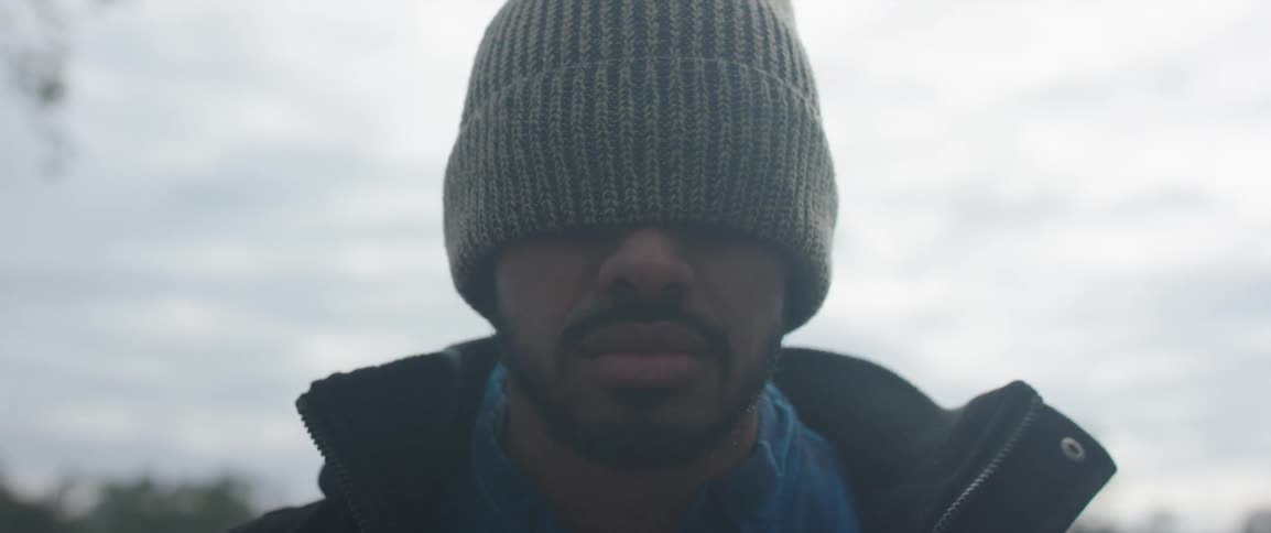 Bearded man wearing a beanie hat over his eyes standing in front of the camera outdoors