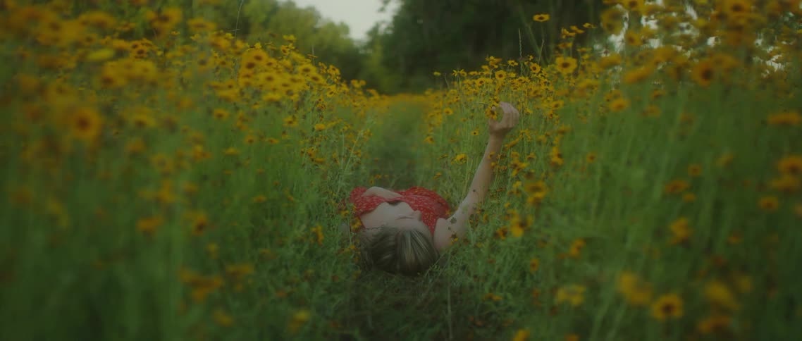 A woman in a red outfit lies on her back in a field of flowers