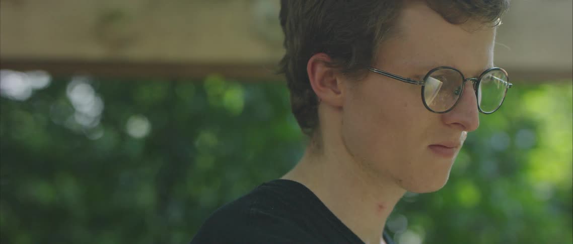A male teenager stands in front of greenery during the day