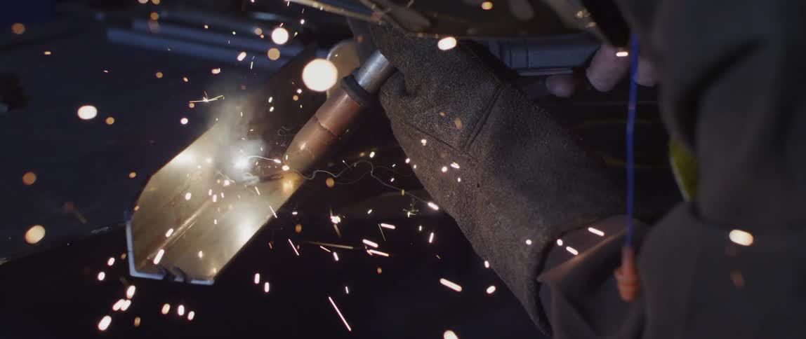 A person is welding a piece of metal while wearing safety gloves and face protection