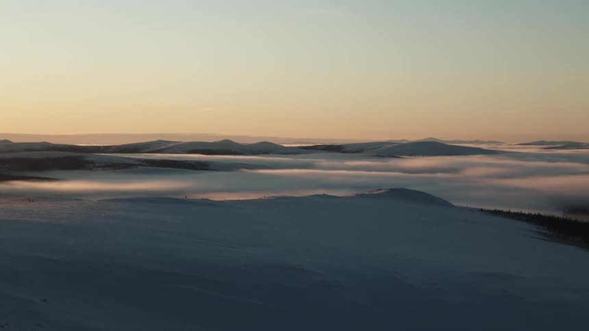 A landscape view of snow covered hills as the sun rises