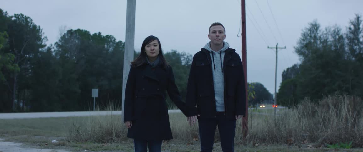 Young couple holding hands looking at the camera standing near a road outdoors at evening