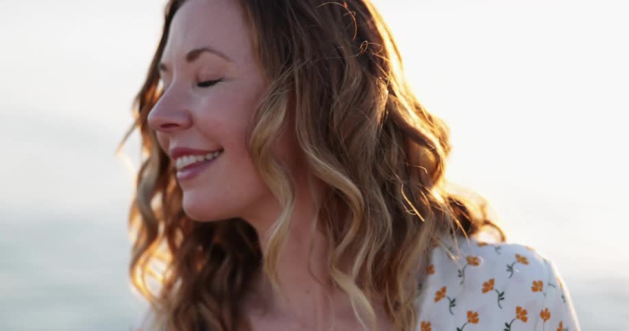 A woman with a nose ring and wearing a floral top stands outdoors smiling