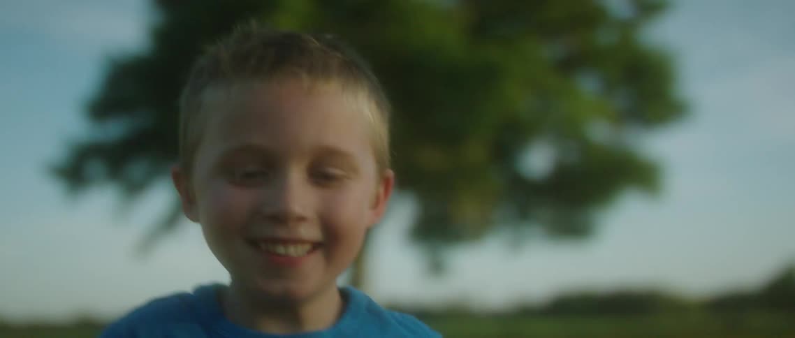 A young blonde boy smiling while running in a grassy field on a summer day