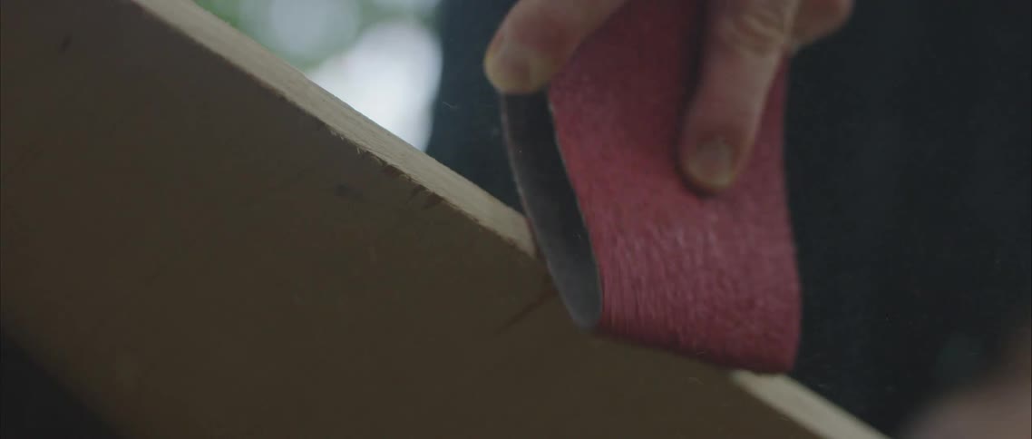 Close up of a mans hand as he sands wood