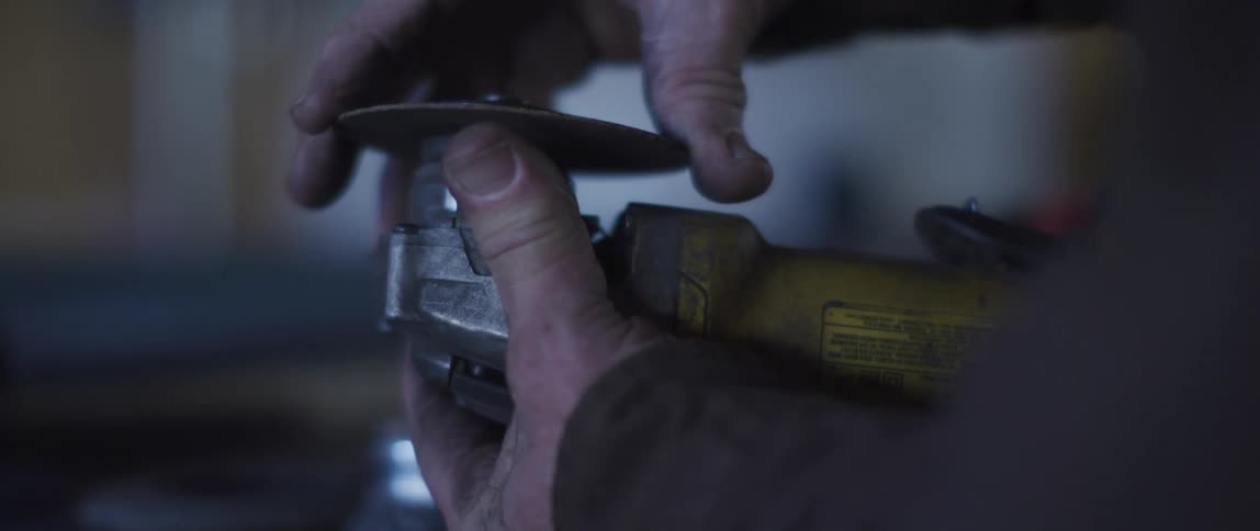 A person in a room turning a bolt on an electric sander