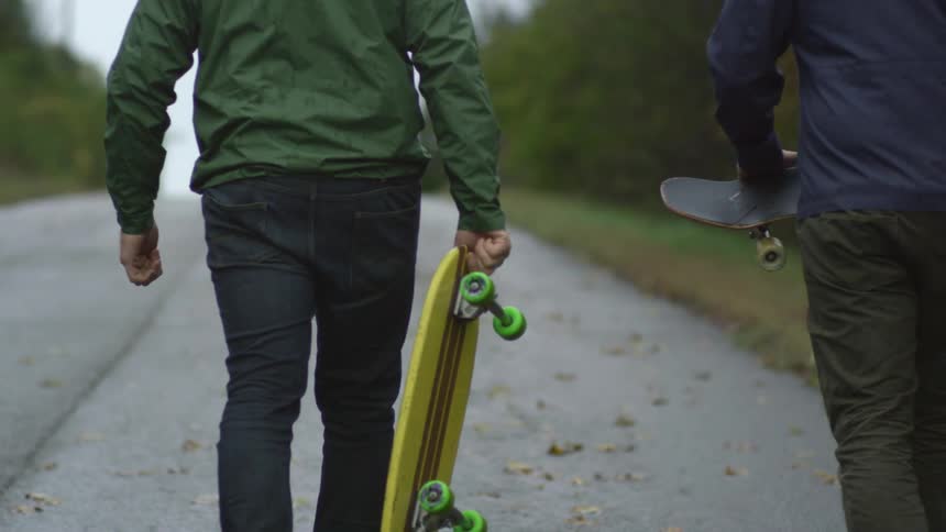 Two men walking up a hill with skateboards
