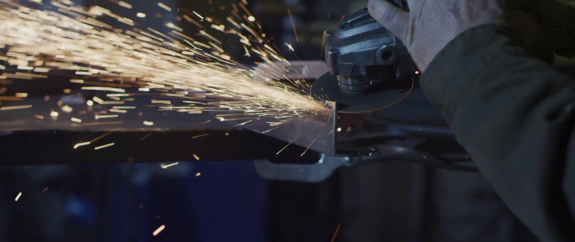 Sparks fly as a man uses a grinder saw on a piece of metal in his garage