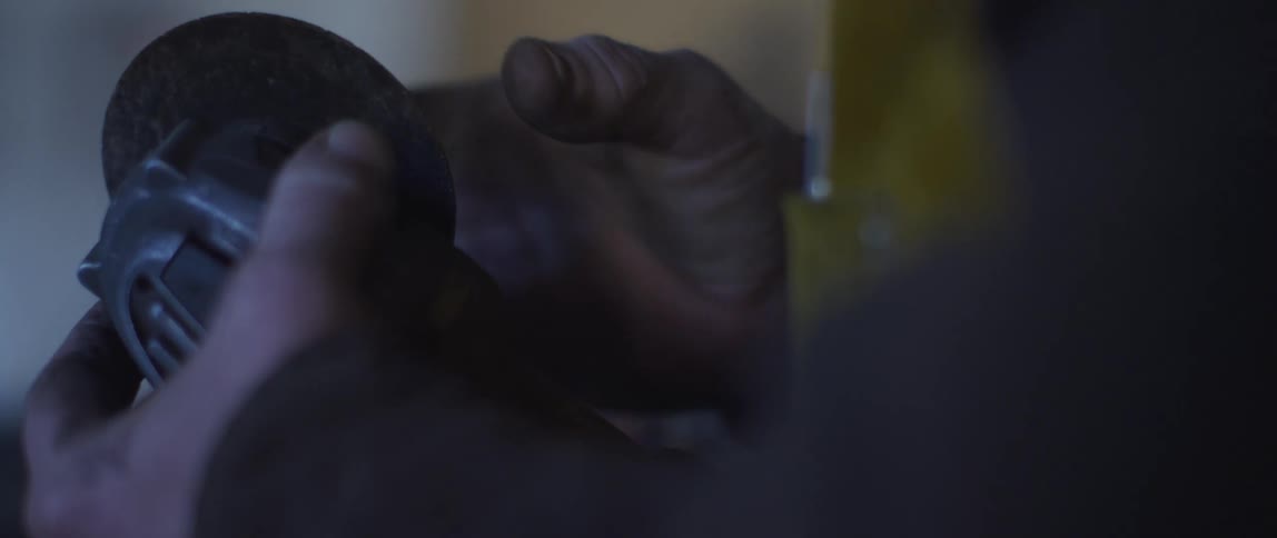 A man with dirty hands fixes an electric power tool in a dimly lit room