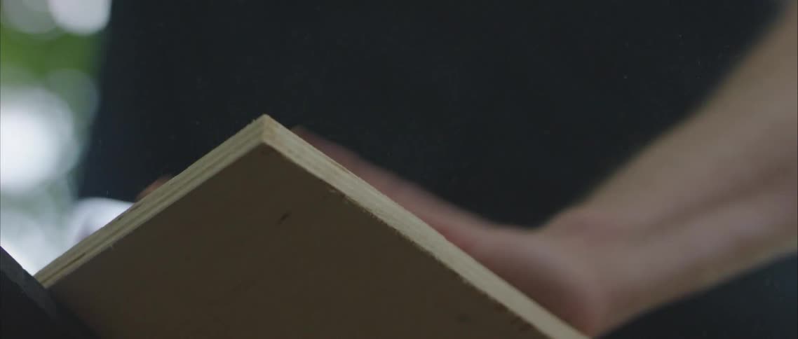 A manin a black tee shirt dusting off a wood board outside