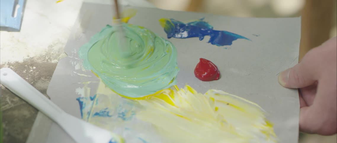 A person with a paintbrush mixing paint on a piece of cardboard