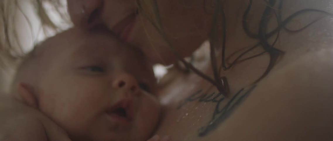 A young mother rests her mouth on her babies head as she holds it close to her chest