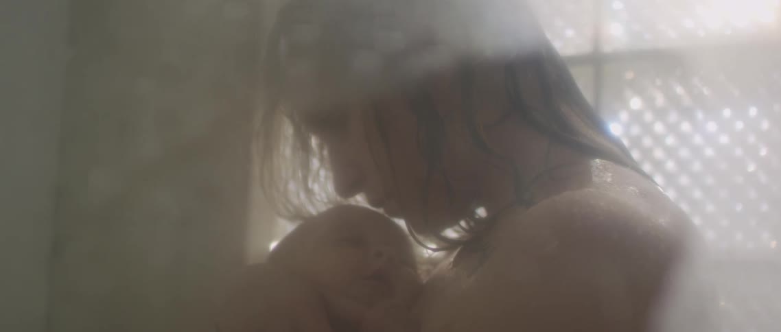 Mother holding a baby under the shower in the bathroom at home
