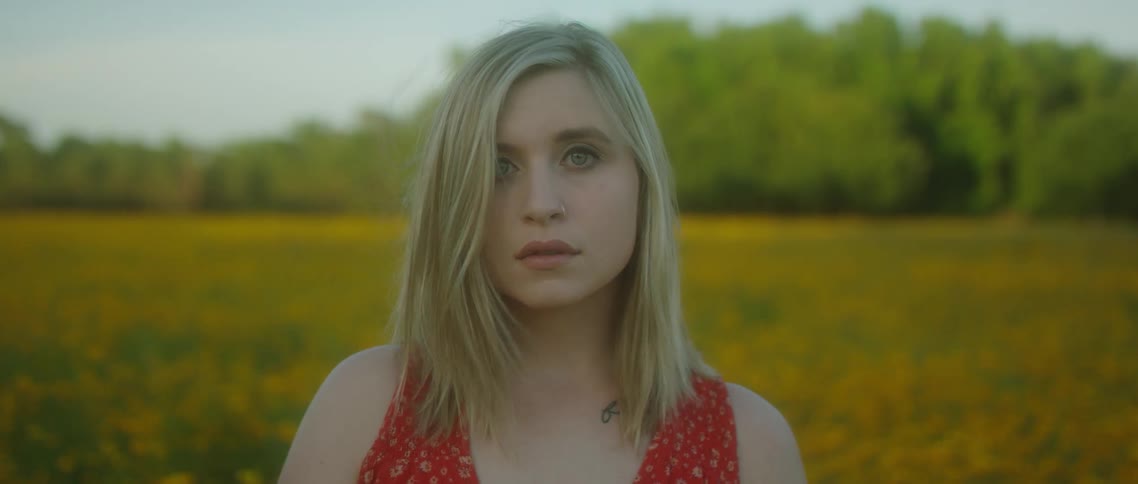 Young blonde woman looking at camera standing in a flower field at day time