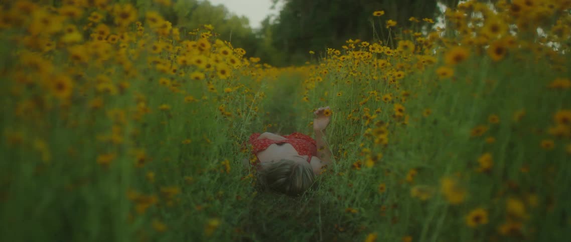 Young woman in a red dress laying on a field of yellow flowers at day time