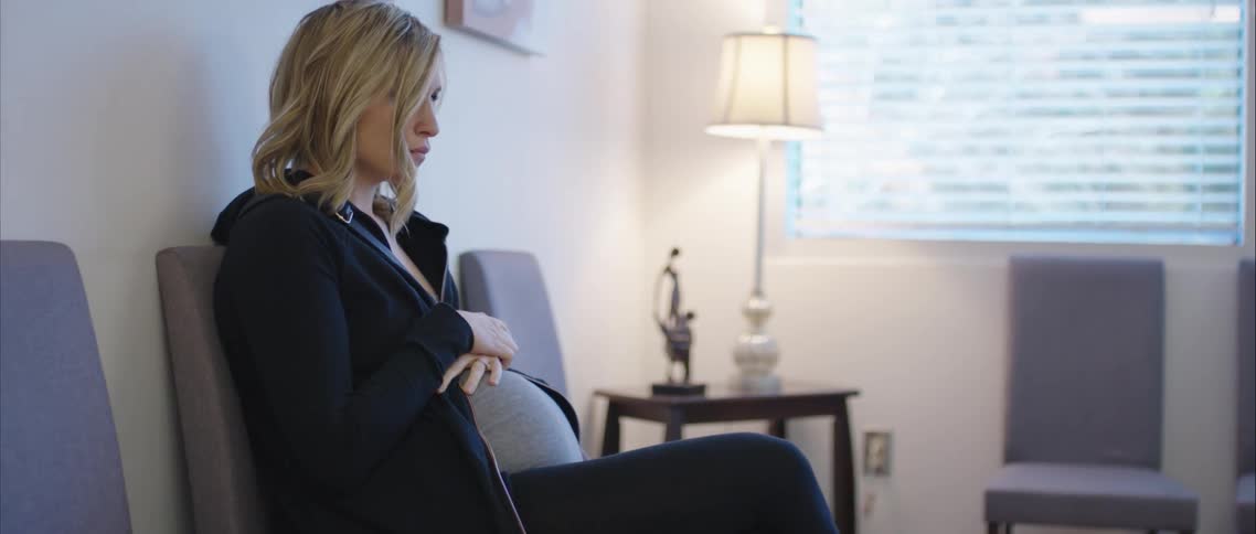 A pregnant woman sitting in a waiting room with her hands on her stomach