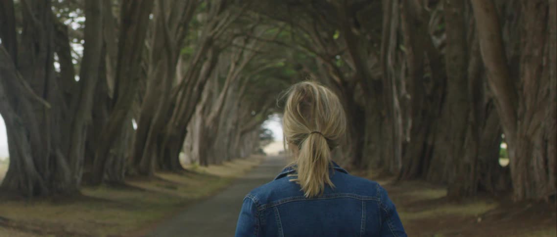 A woman walking on a pathway surrounded by trees with the sky and clouds in the background