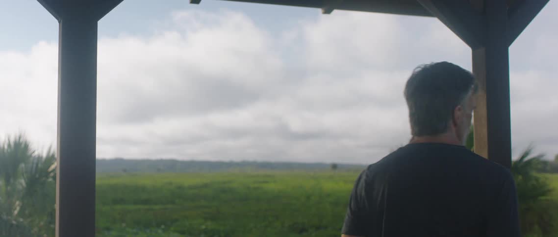 Man standing on the porch looking at the green grass fields at day time
