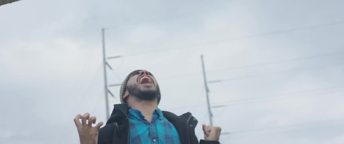 A man standing outside screams and throws up his fists in frustration