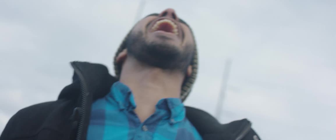 A man dressed in cold weather clothing shouts at the cloudy daytime sky