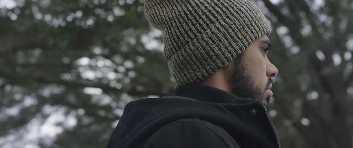 A man in a winter hat and coat standing outside beneath trees