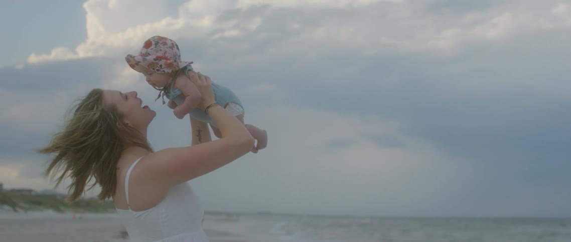 A mother holding up a baby on a windy beach