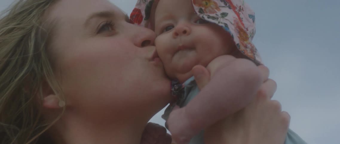 A young mother smiling and kissing a baby in a sunhat