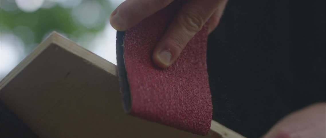 Carpenter uses sand paper to sand the corners of a wooden board outdoors