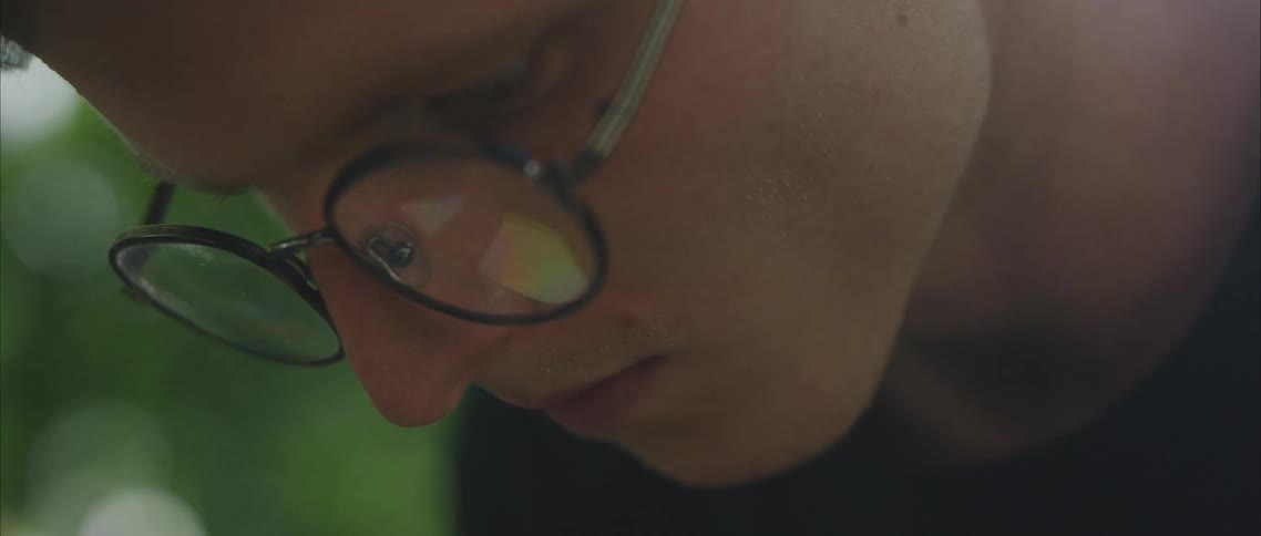 A man outdoors wearing glasses and looking down