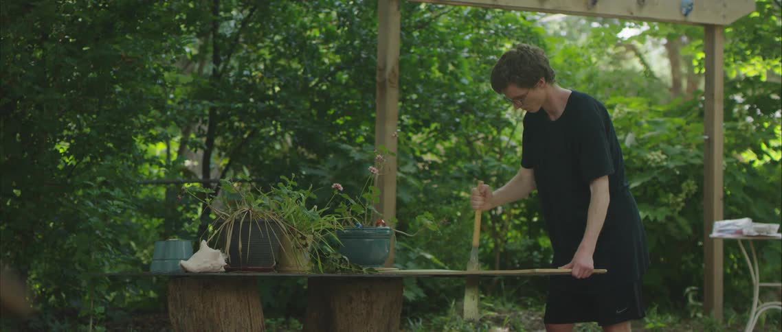 A man with glasses using a tool with plants and trees in the background
