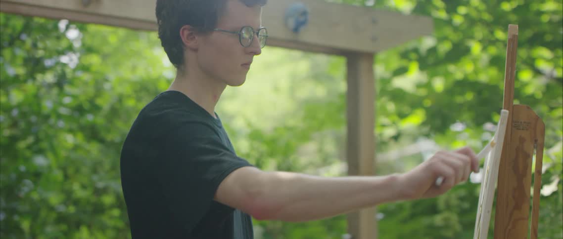 A teenage boy paints on a canvas in his back yard