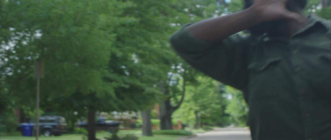 A large man dances in the center of a road through a residential neighborhood during the day