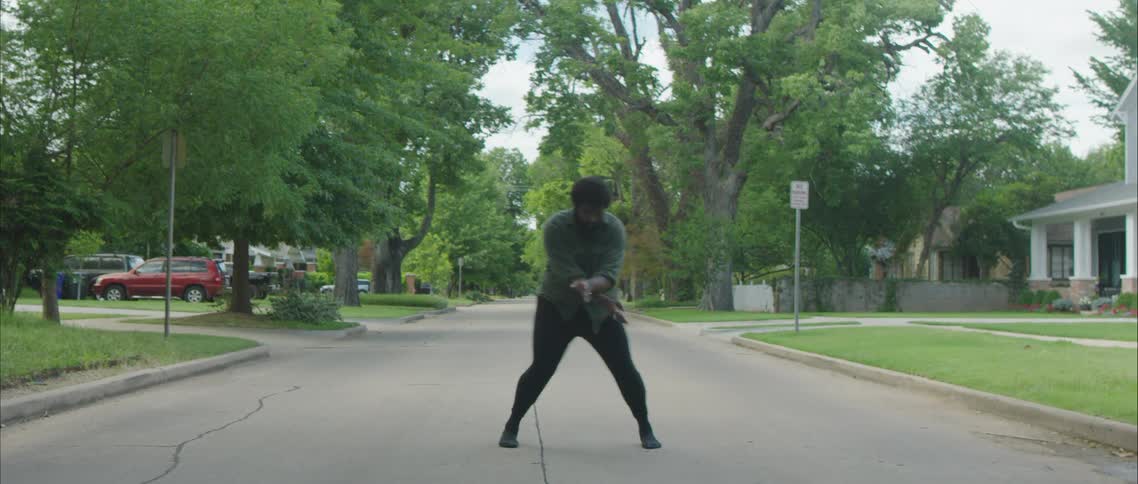 A man dancing on a residential street on a summer day