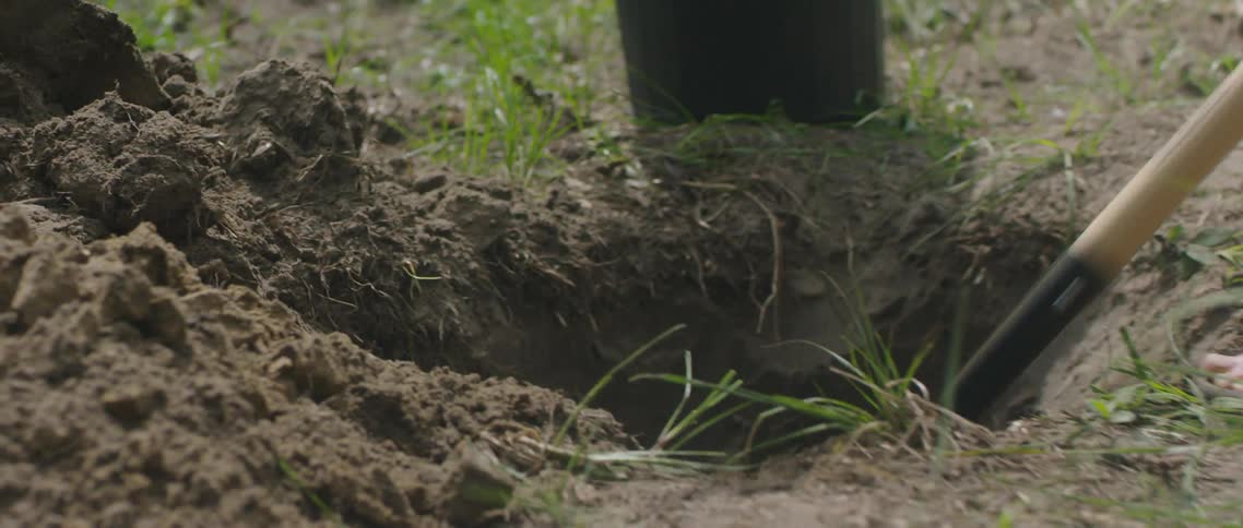 A person digging a hole in the dirt using a shovel outdoors at day time
