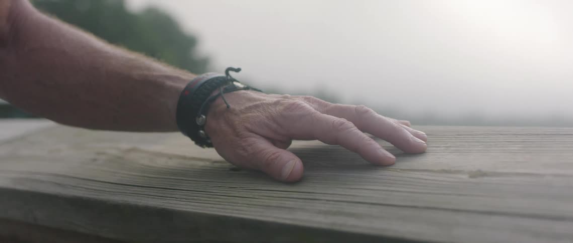 A person rubbing their hand on a piece of wood with trees the sky and clouds in the background