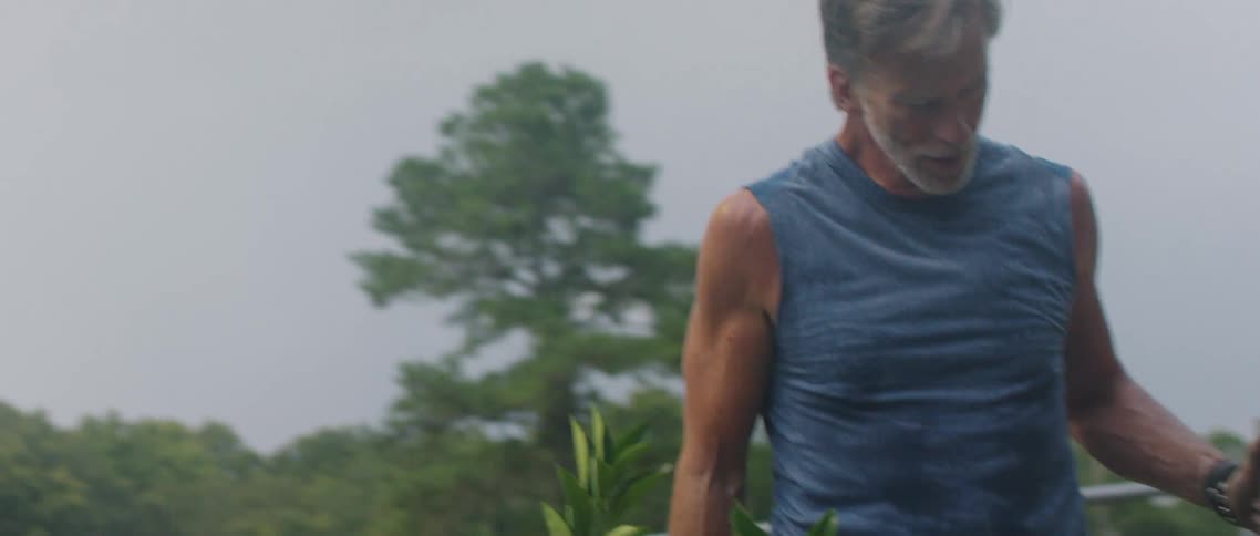 A man stops and takes a step back while gardening to wipe sweat off his brow